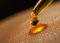 CBD-Öltropfen auf Pipette über Hautoberfläche in Makroaufnahme