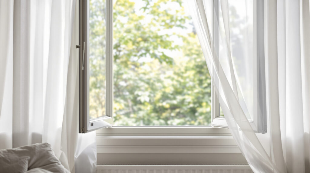 Geöffnetes Fenster mit wehenden Vorhängen in Wohnraum