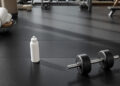 Hantel und Wasserflasche auf Gummiboden im Fitnessstudio