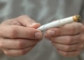 Junge männliche Hand hält gedrehten Cannabis-Joint vor unscharfem Hintergrund