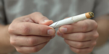 Junge männliche Hand hält gedrehten Cannabis-Joint vor unscharfem Hintergrund