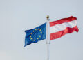EU- und Österreich-Flagge nebeneinander vor grauem Himmel