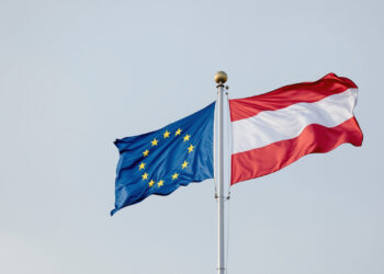 EU- und Österreich-Flagge nebeneinander vor grauem Himmel