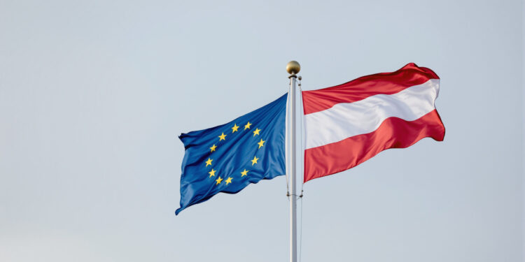 EU- und Österreich-Flagge nebeneinander vor grauem Himmel
