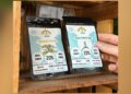 Zwei Packungen Cannabis-Samen in einem Holzregal, eine Hand greift danach