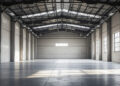 Leere Industriehalle mit Betonboden und Tageslicht durch große Fenster